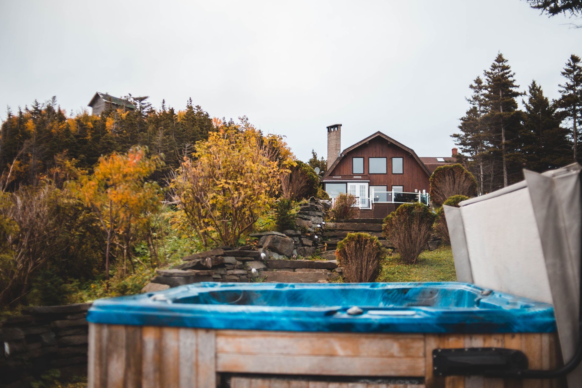A serene countryside house surrounded by autumn foliage with a hot tub in the foreground.