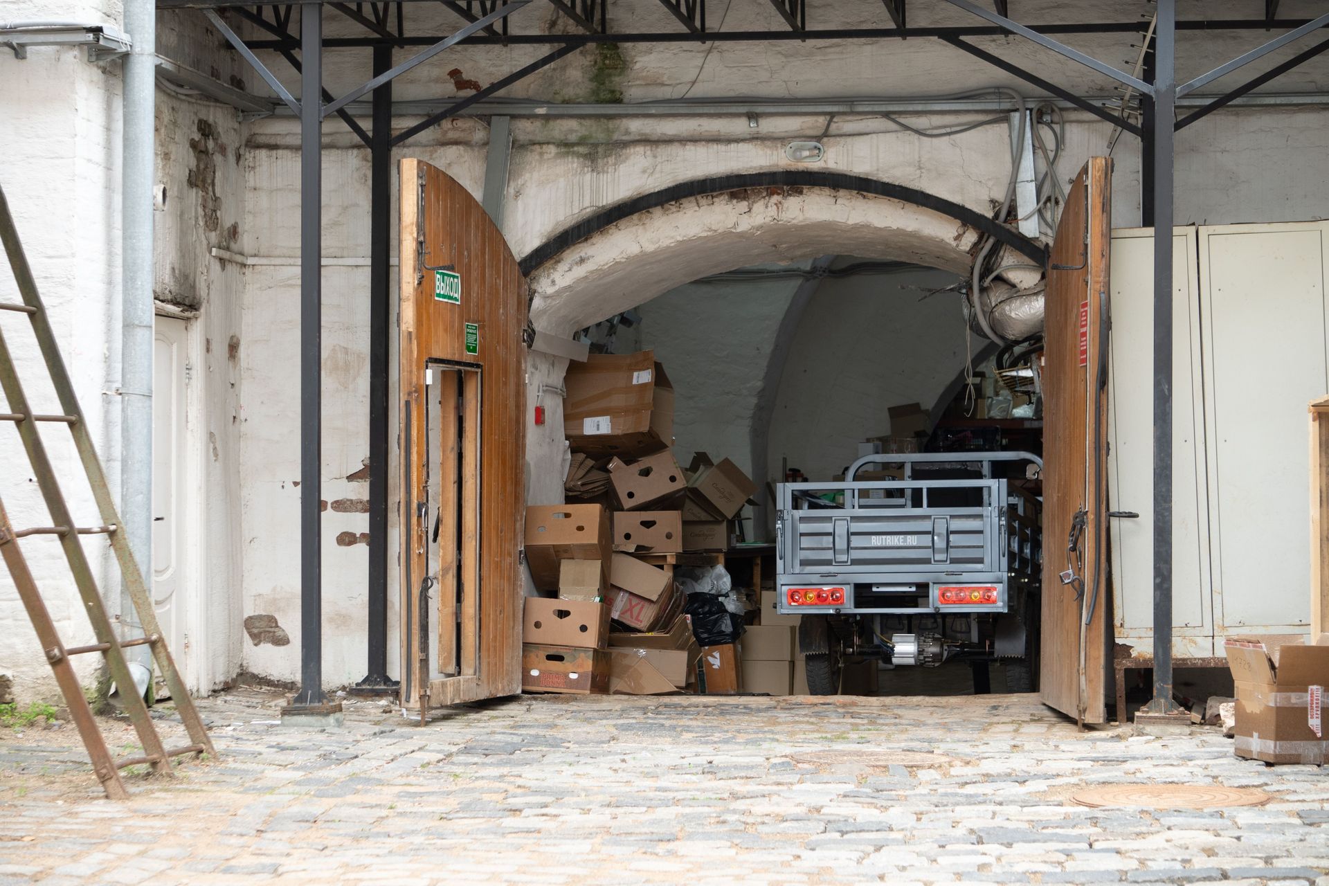 Warehouse entrance with cardboard boxes and open wooden doors, a vehicle partially visible.