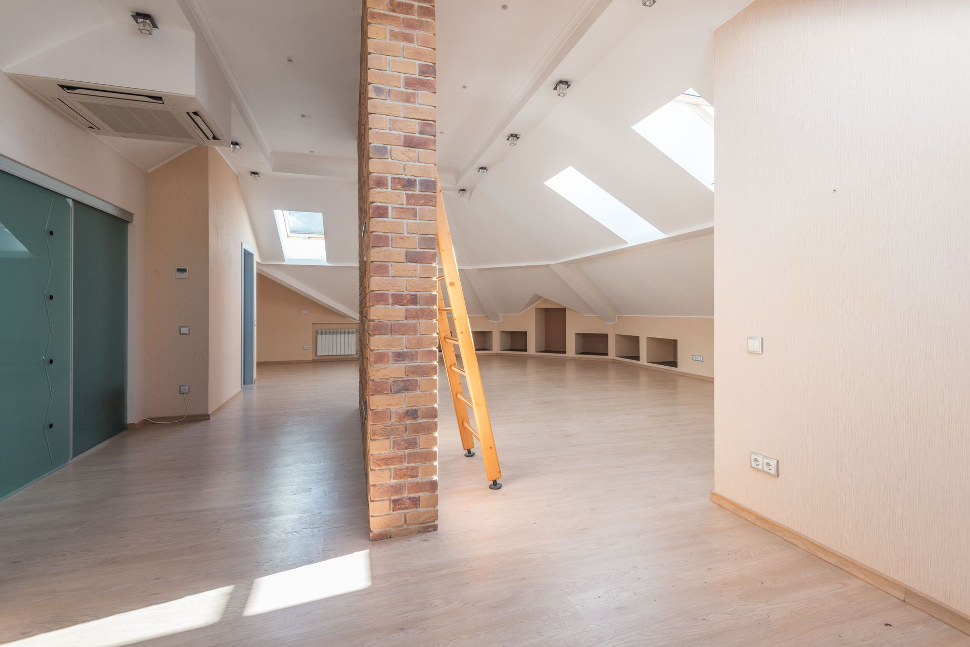 Spacious attic room with natural light from skylights, featuring a brick pillar and a wooden ladder.
